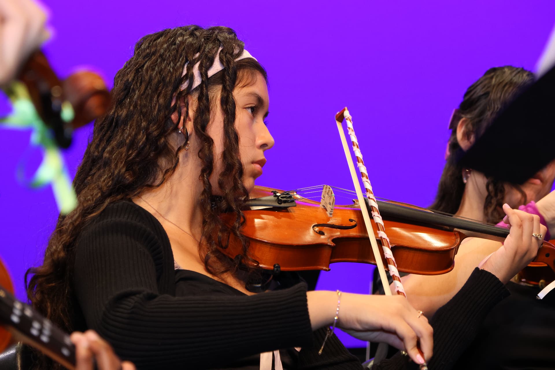 A young violinist of the Youth Symphony Orchestra playing in profile against a violet backdrop