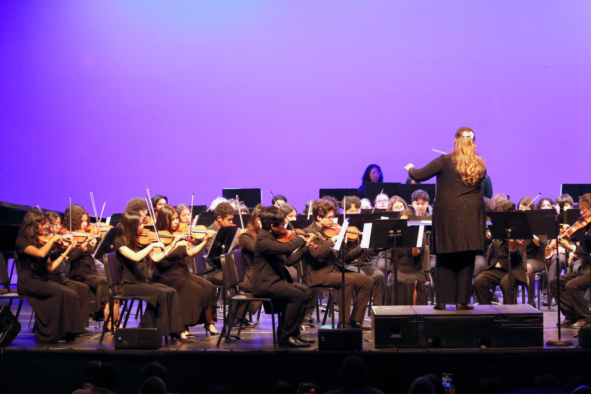 The Youth Symphony Orchestra on stage under violet light, the conductor on the podium at the right