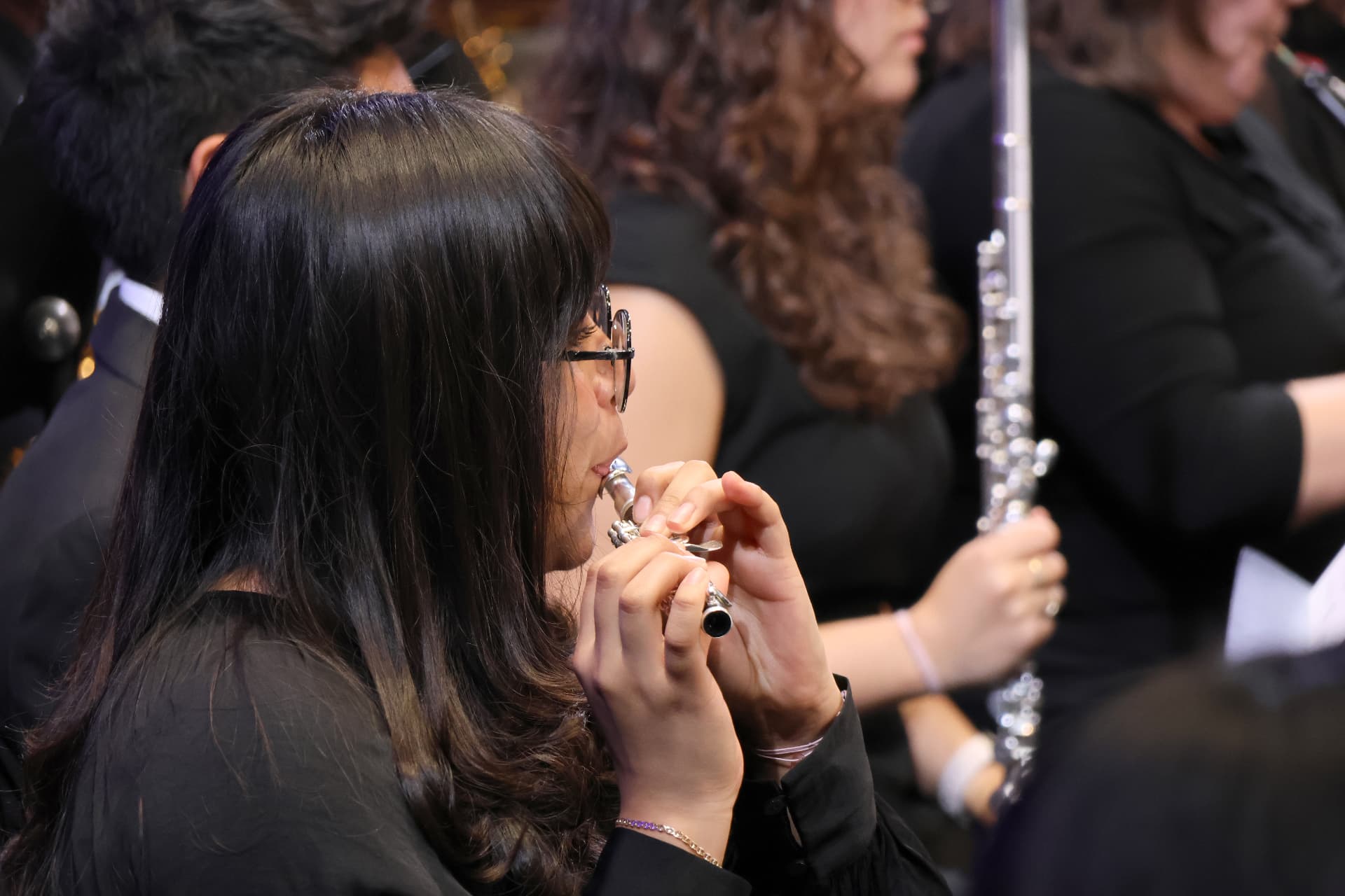 A young flutist wearing glasses plays the piccolo in the woodwind section